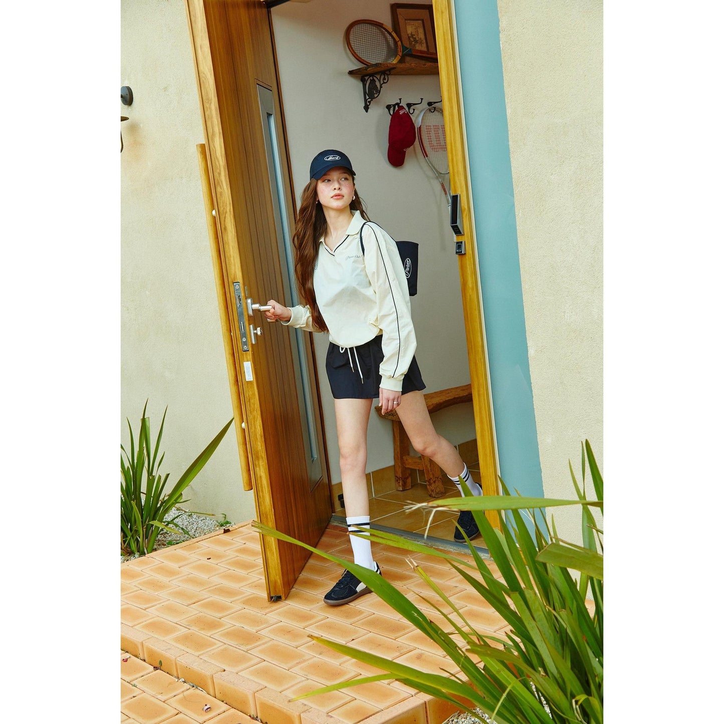 model wearing piv'vee club piste top with stylish shorts and accessories, standing at a door entrance