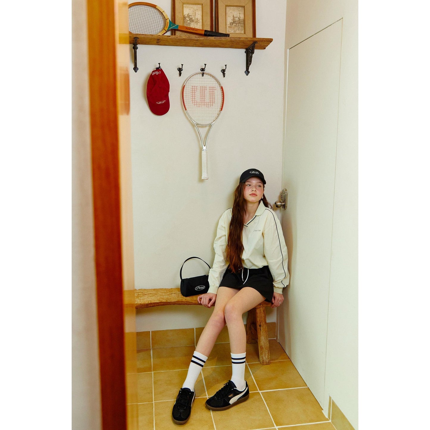 young woman in stylish outfit with piv'vee club piste top sitting in sports-themed hallway